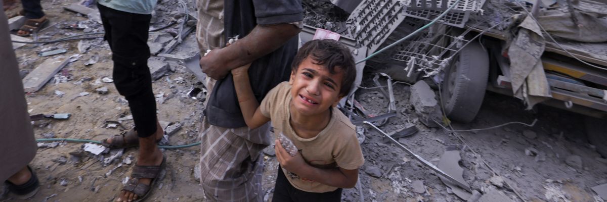 A Palestinian man covered in dust holds the hand of a weeping child