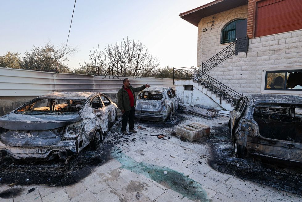 A Palestinian man stands amid torched cars near a house in Huwara. 
