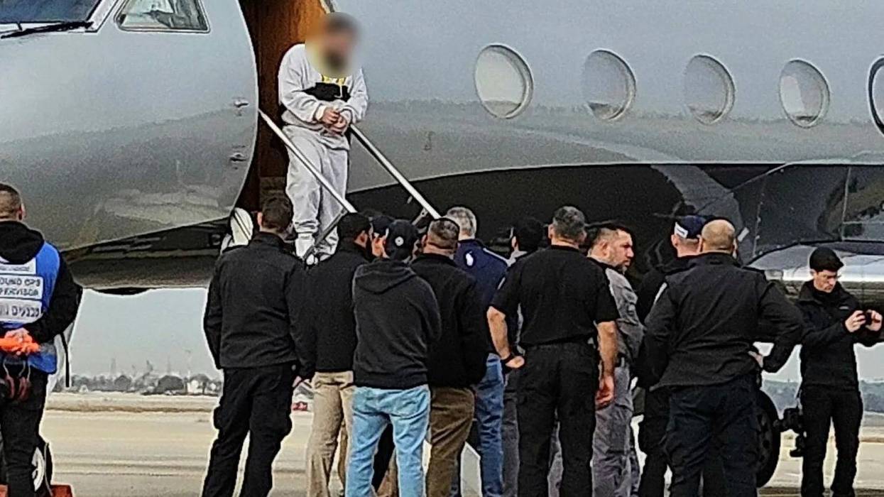 A Palestinian man with his hands bound steps off the private jet