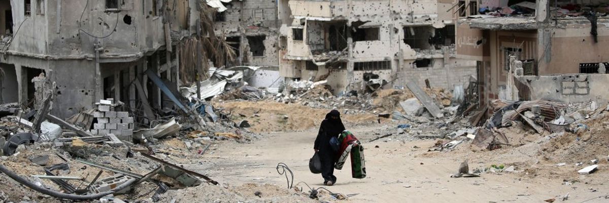 A Palestinian woman carries belongings through bombed-out Gaza