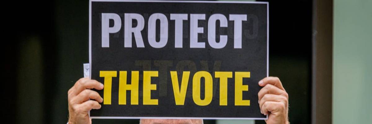 A participant holding a Protect The Vote sign outside NBC