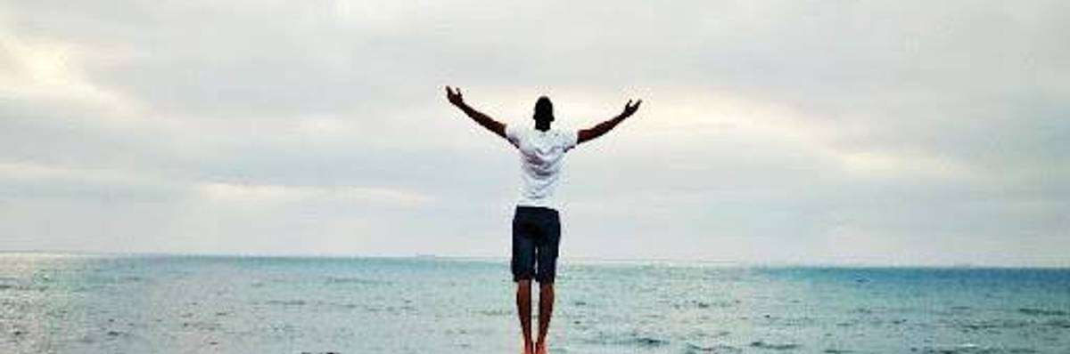 A person faces the ocean with their arms outstretched.