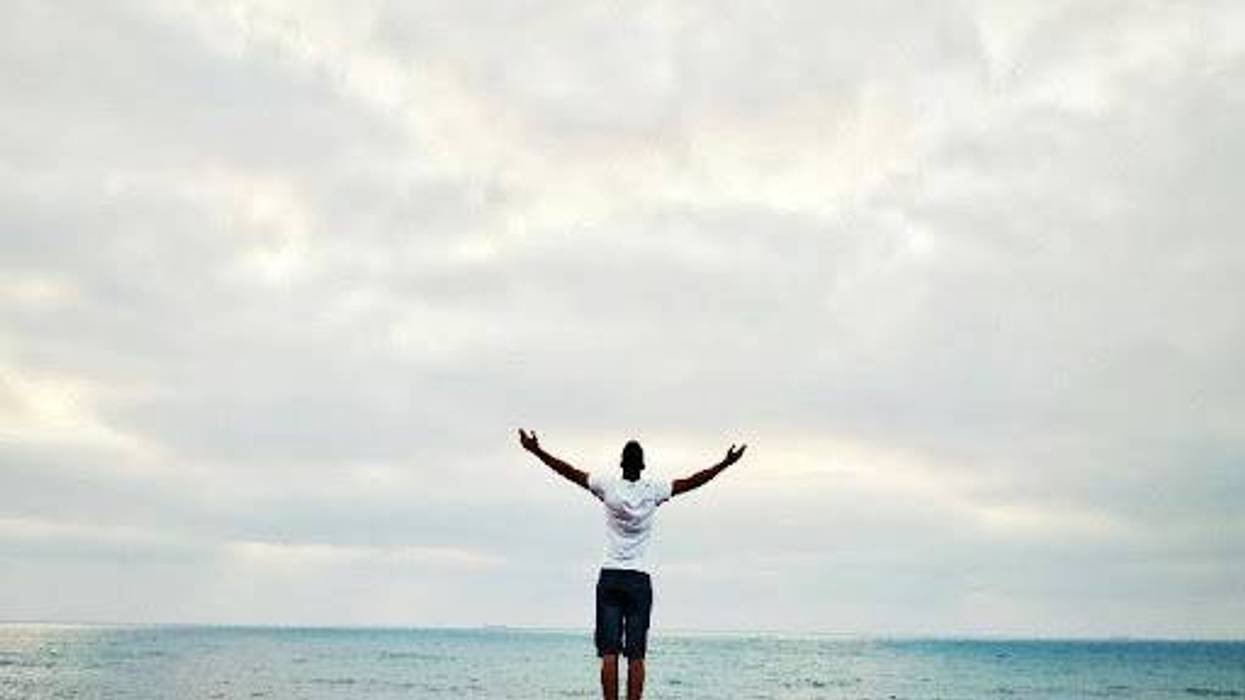 A person faces the ocean with their arms outstretched.