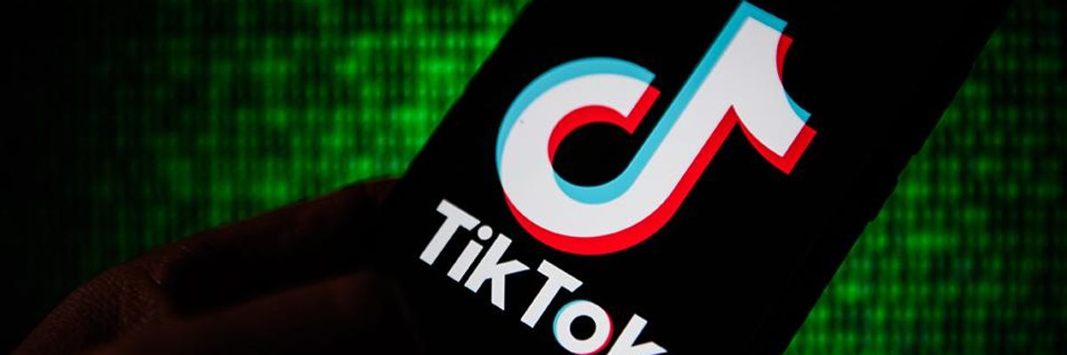 A person holds a phone displaying the TikTok logo against a green background. 