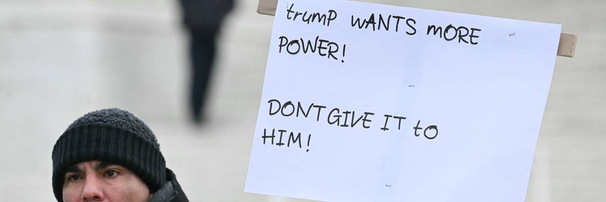 A person holds a sign in front of the Supreme Court reading, "Trump wants more power! Don't give it to him!"