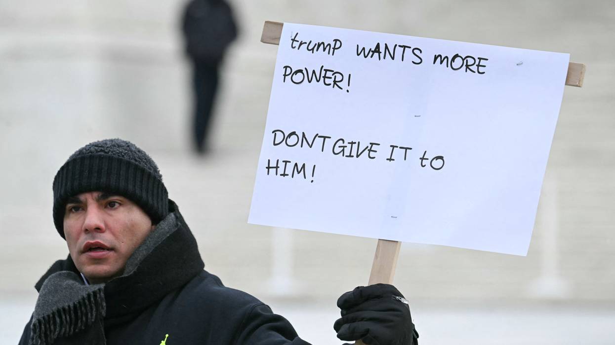 A person holds a sign in front of the Supreme Court reading, "Trump wants more power! Don't give it to him!"