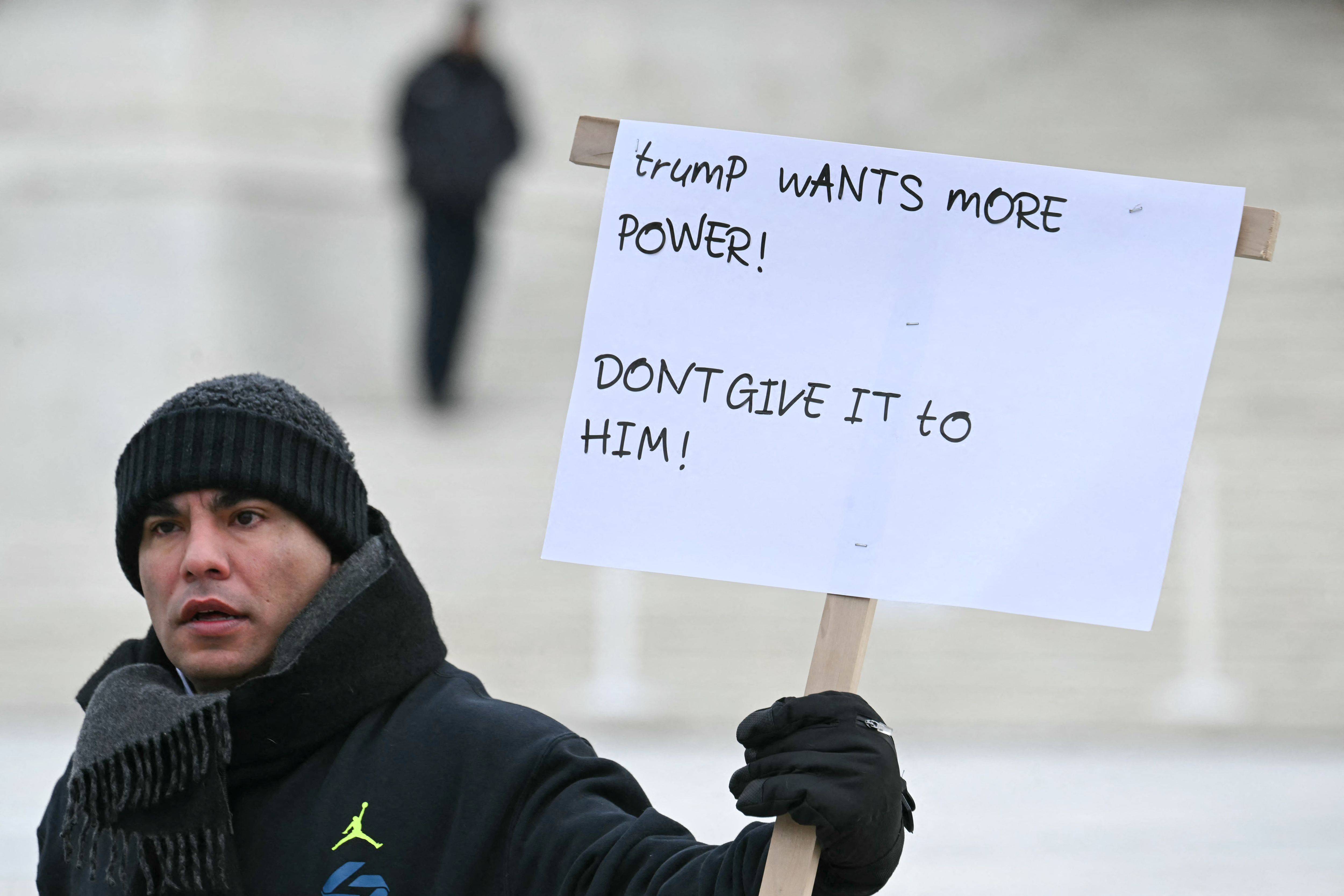 A person holds a sign in front of the Supreme Court reading, "Trump wants more power! Don't give it to him!"