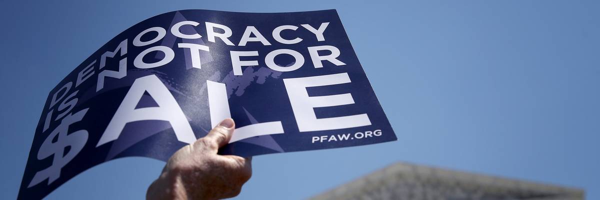 A person holds a sign reading, "Democracy is not for sale."