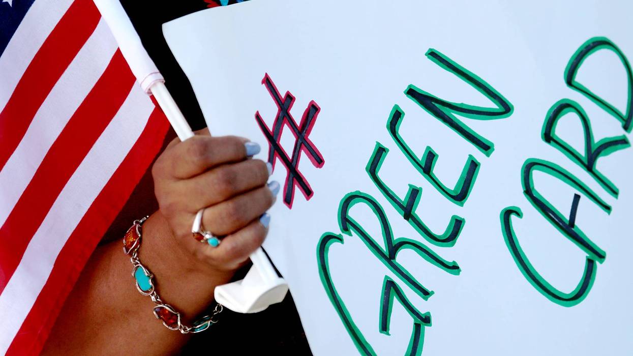 A person holds a sign reading "green card."