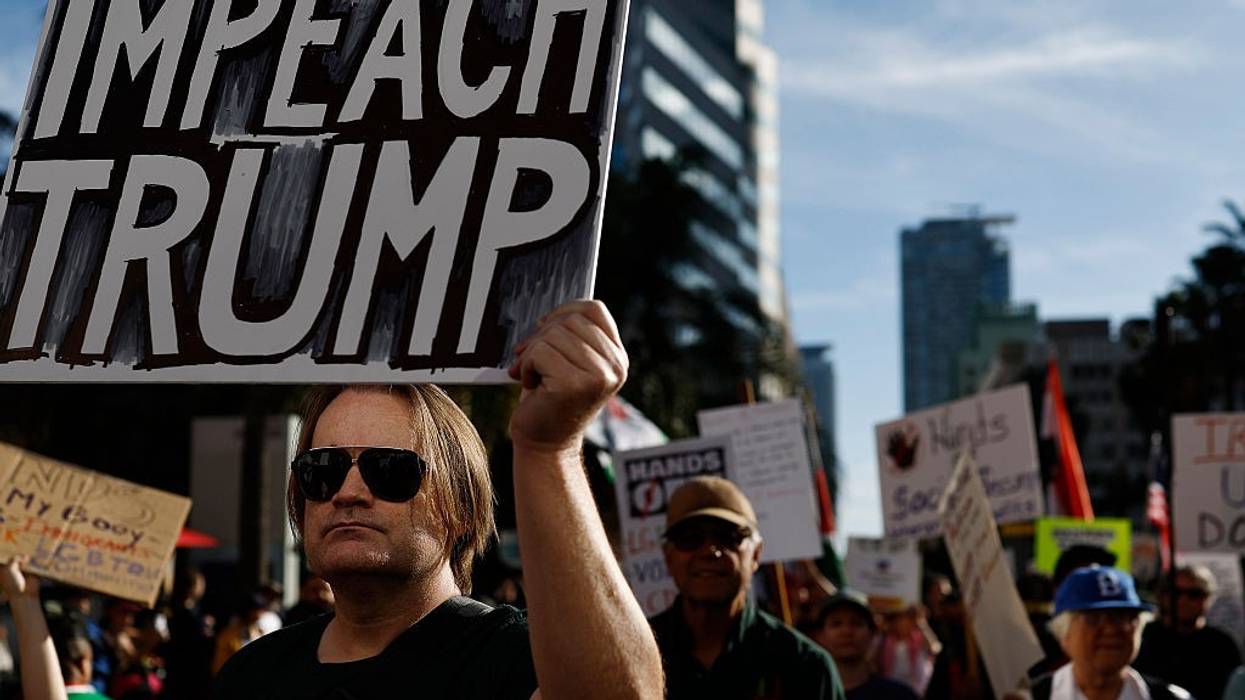 A person holds a sign reading "Impeach Trump" as protestors march
