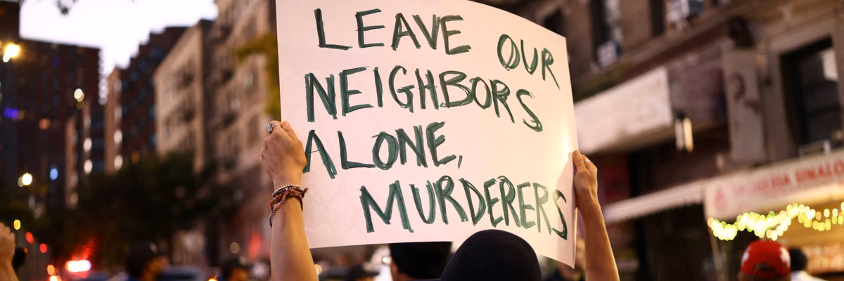 A person holds a sign reading, "Leave our neighbors alone murderers," referring to ICE.