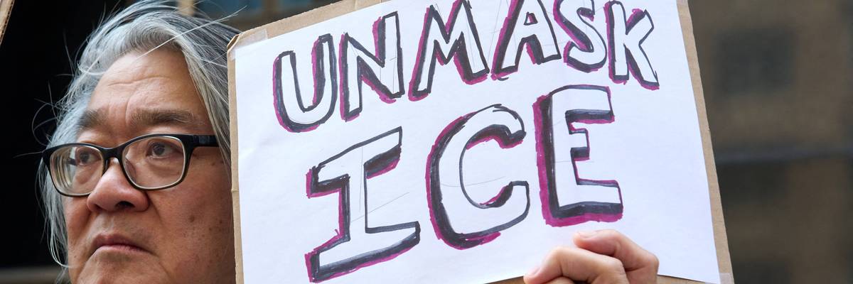 A person holds a sign saying, "Unmask ICE."