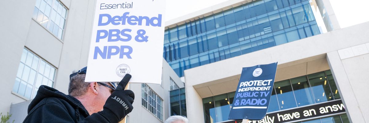 a person holds a sign that says "Defend PBS and NPR"