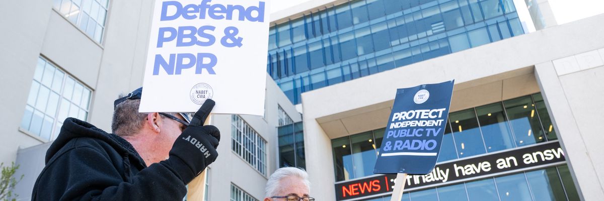 a person holds a sign that says "Defend PBS and NPR"