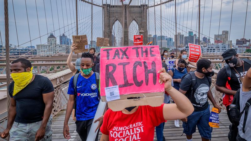 A person holds a Tax The Rich sign at a June 27, 2020 protest march on the Brooklyn Bridge in New York City.