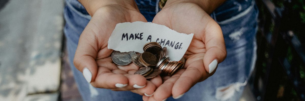 A person holds coins in their hands with a piece of paper reading, "Make a change."