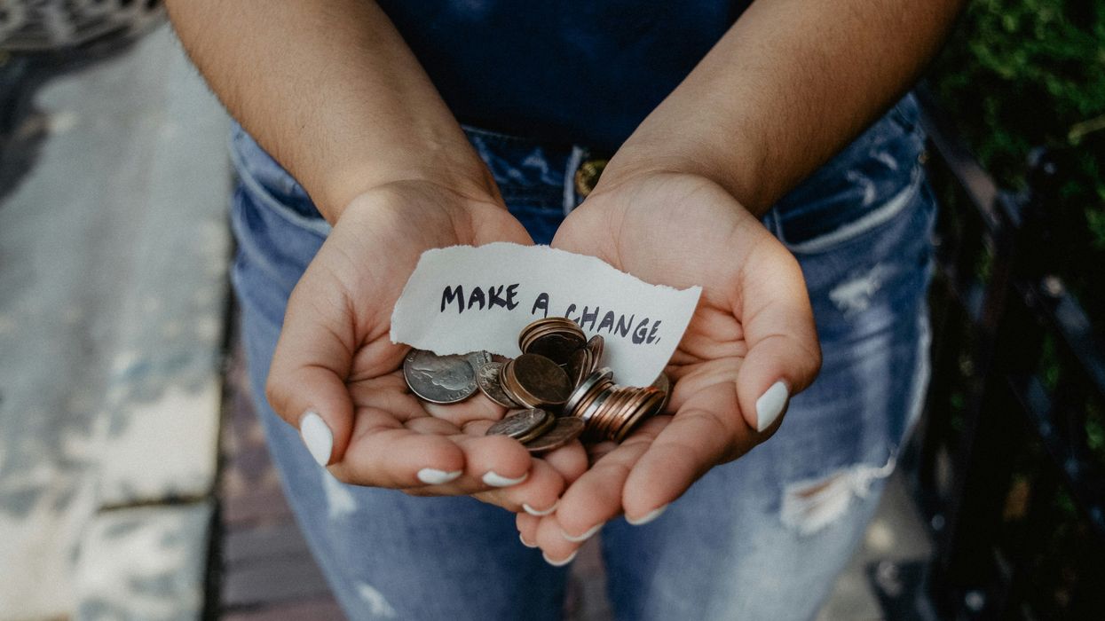 A person holds coins in their hands with a piece of paper reading, "Make a change."