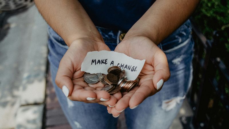 A person holds coins in their hands with a piece of paper reading, "Make a change."