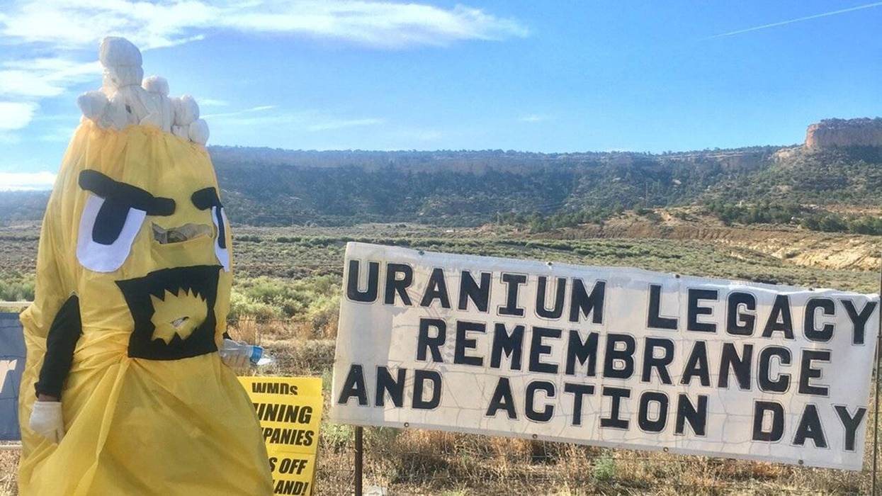 A person in a costume holds a sign reading, "Uranium Legacy Remembrance and Action Day."