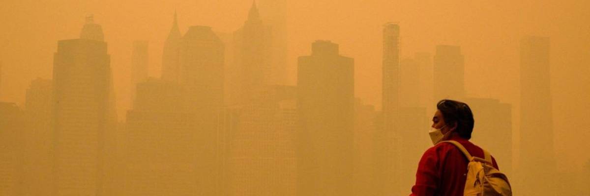 A person in a face mask looks at a smoke-obscured New York City skyline.