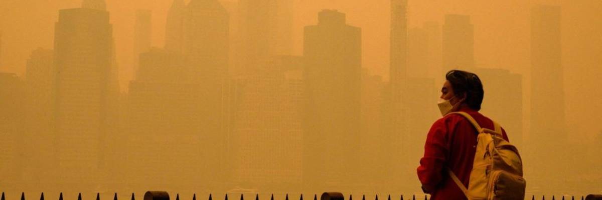 A person in a face mask looks at a smoke-obscured New York City skyline.