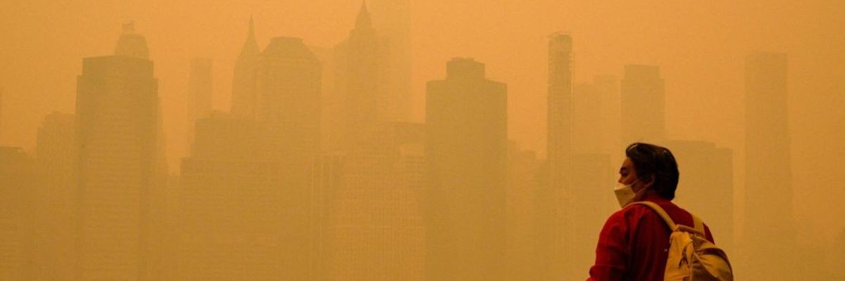 A person in a face mask looks at a smoke-obscured New York City skyline.