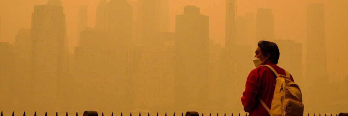 A person in a face mask looks at a smoke-obscured New York City skyline.