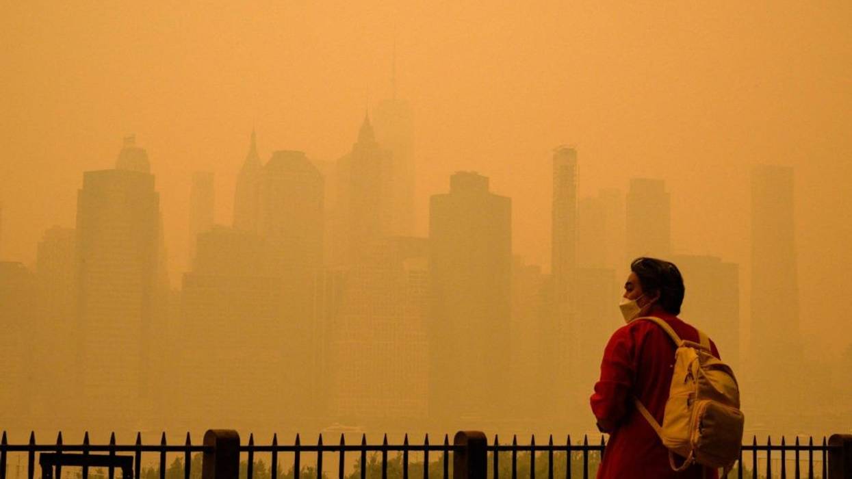 A person in a face mask looks at a smoke-obscured New York City skyline.