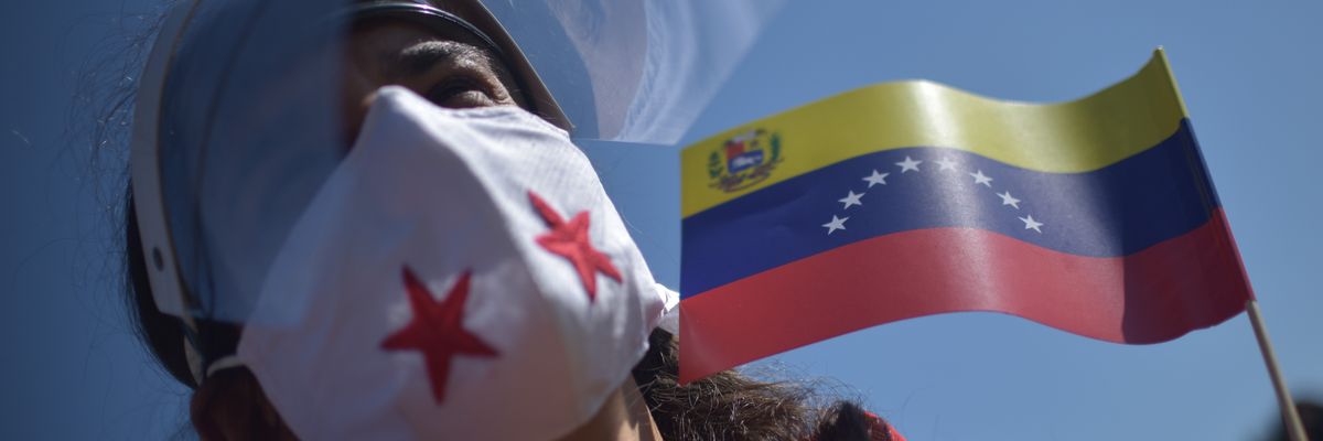 A person in a facemask holds a Venezuelan flag.