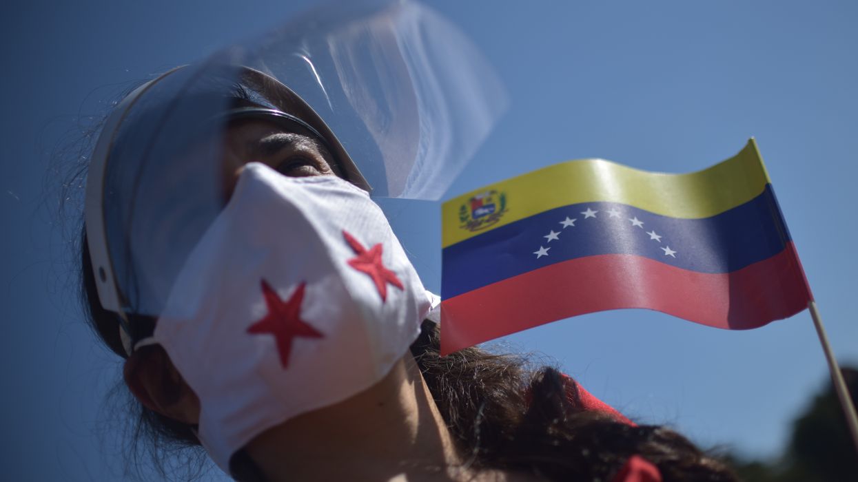 A person in a facemask holds a Venezuelan flag.