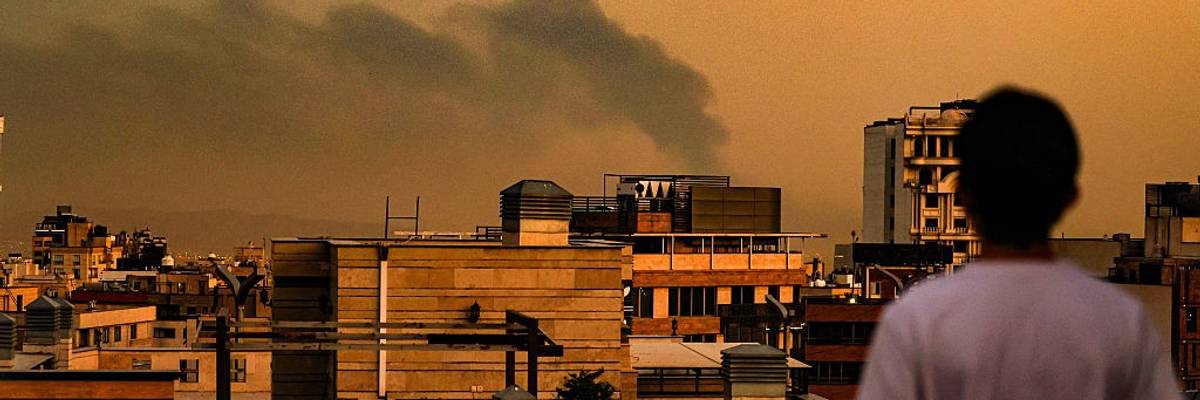 A person looks at Tehran's smoke-filled skyline following Israeli bombing.