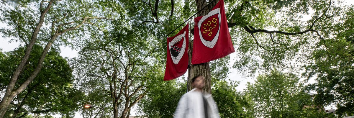 a person not in focus walks in front of two flags