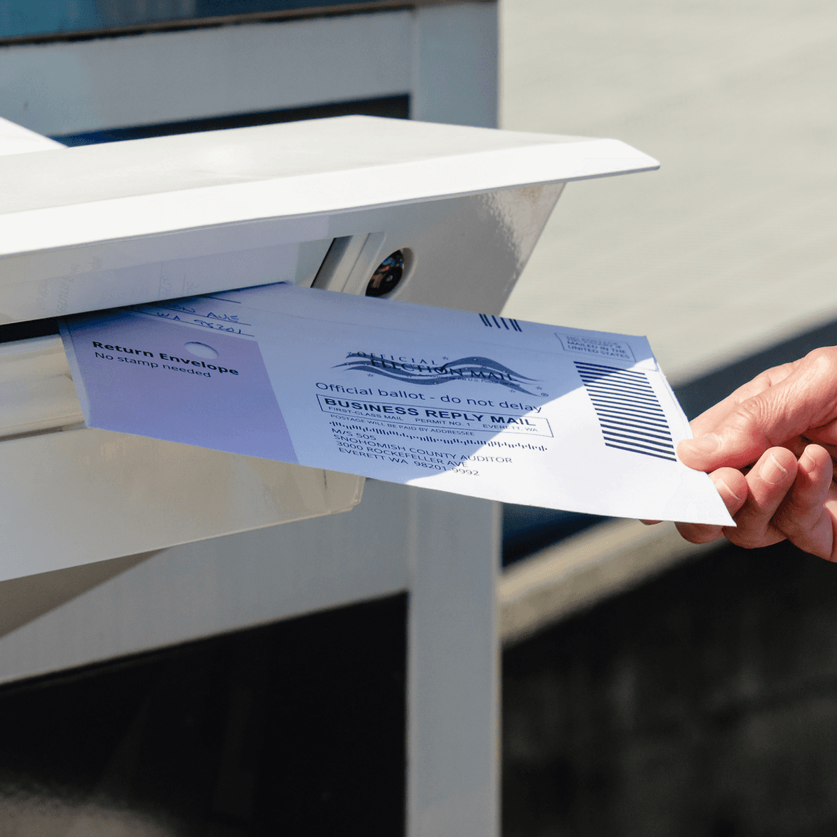 a person places a ballot in a madilbox