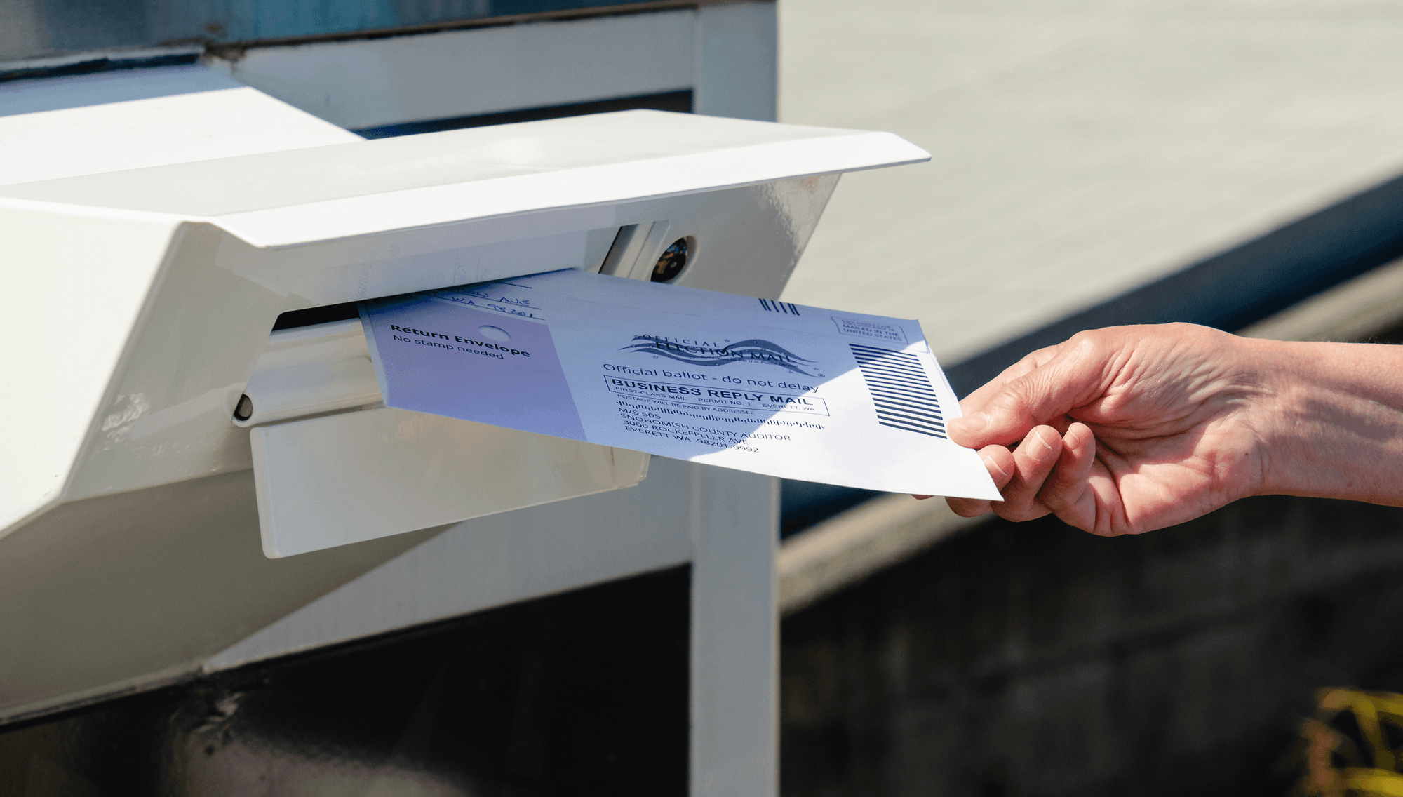 a person places a ballot in a madilbox