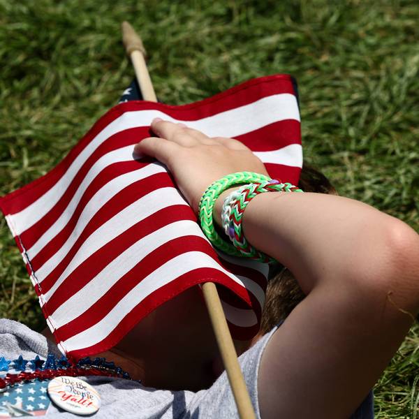 A person shelters from the heat with a US flag.