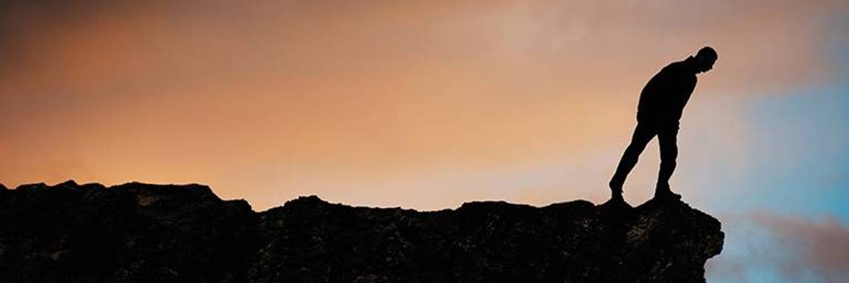 A person stands at the edge of a cliff looking over.