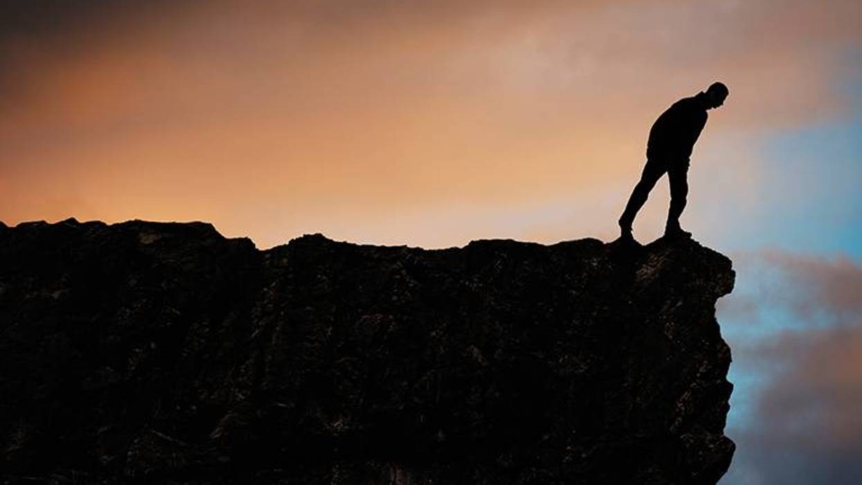 A person stands at the edge of a cliff looking over.