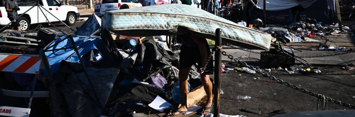 A person walks stooped over carrying a mattress from a tent in a heatwave.