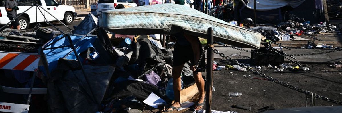 A person walks stooped over carrying a mattress from a tent in a heatwave.