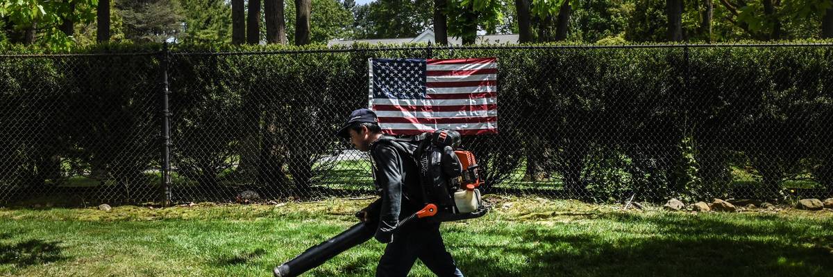A person working as a leaf blower walks past an American flag on May 27, 2020 in Old Westbury, New York. (Photo by Stephanie Keith/Getty Images)
