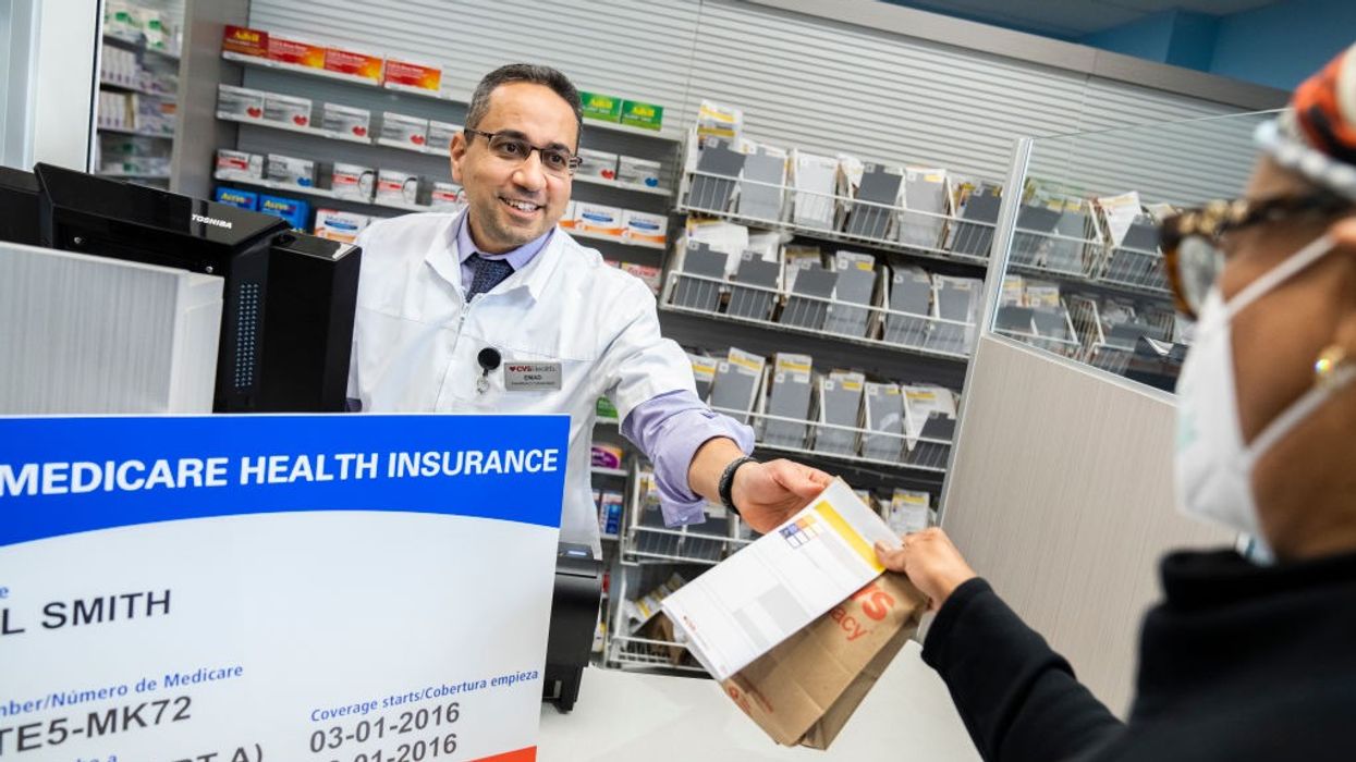 A pharmacist hands a customer her prescription in a brown paper bag