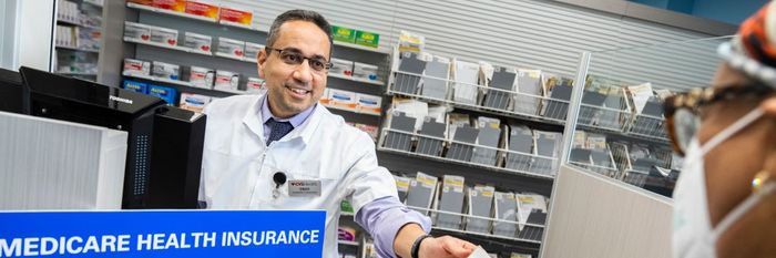 A pharmacist hands a customer her prescription in a brown paper bag