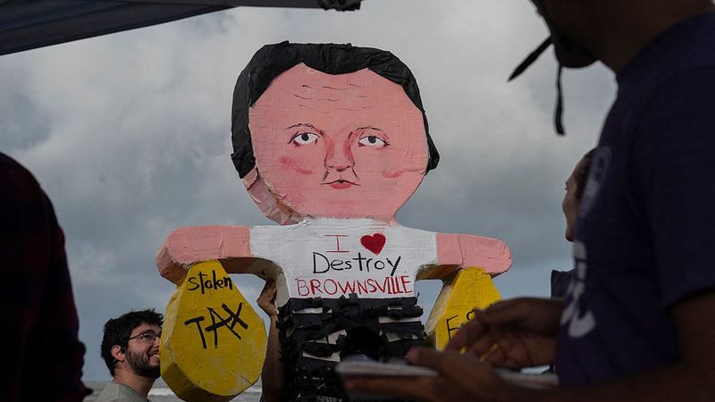 A piñata of Elon Musk wearing a shirt saying, "I love destroy Brownsville" and holding money bags.
