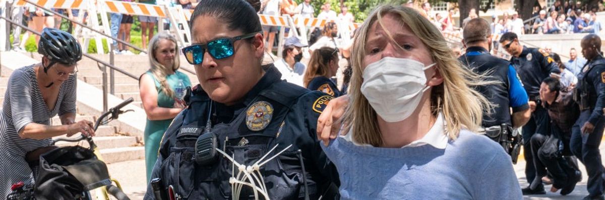 A policewoman arrests a pro-Palestinian proteste; she's wearing a mask and looks distressed