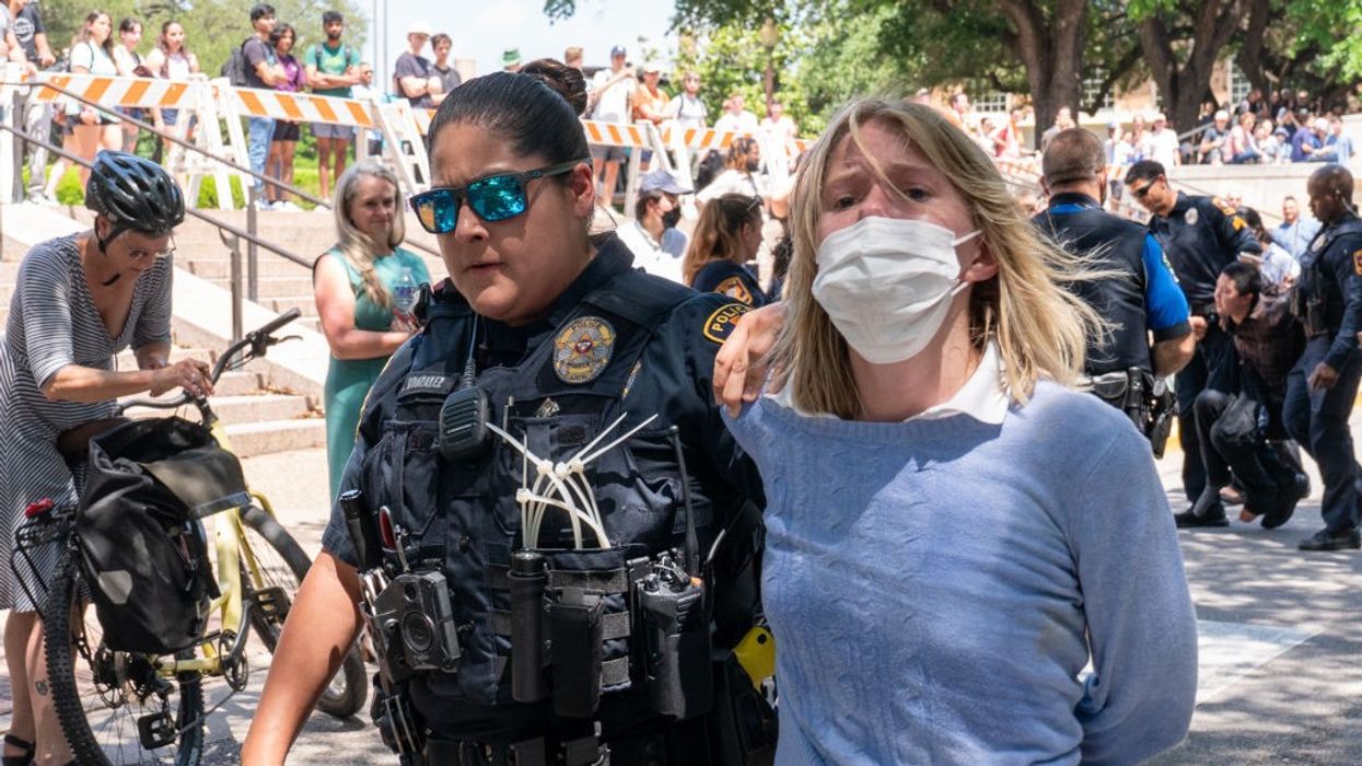 A policewoman arrests a pro-Palestinian proteste; she's wearing a mask and looks distressed