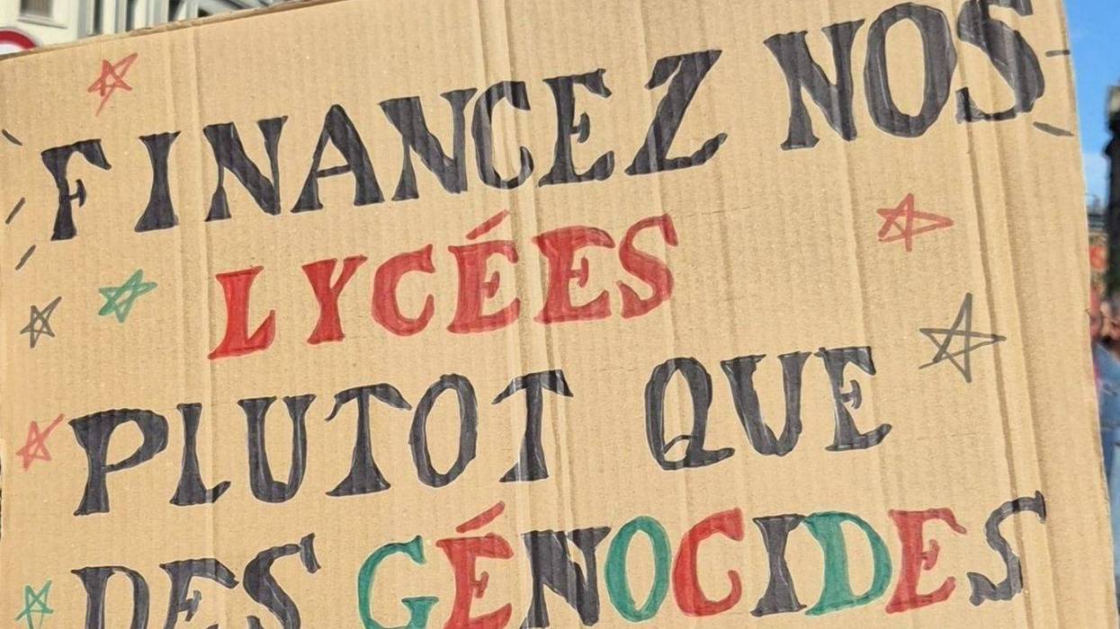 A poster reads, "Fund our high schools instead of genocides," in French.