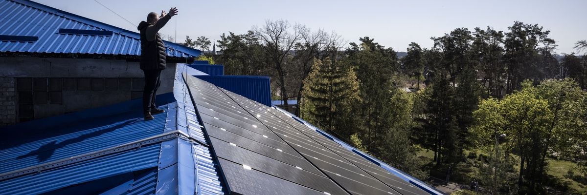 A principle waves to colleagues from a roof in Ukraine covered in solar panels.
