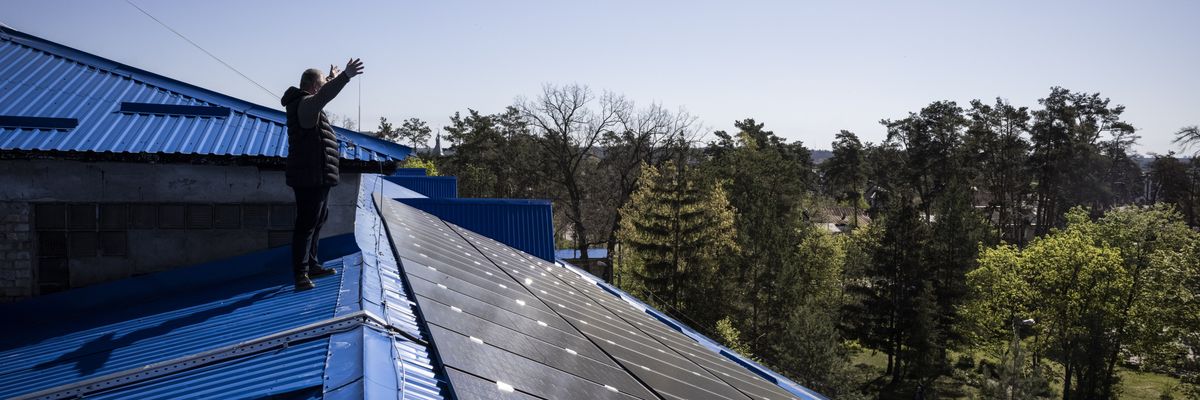 A principle waves to colleagues from a roof in Ukraine covered in solar panels.