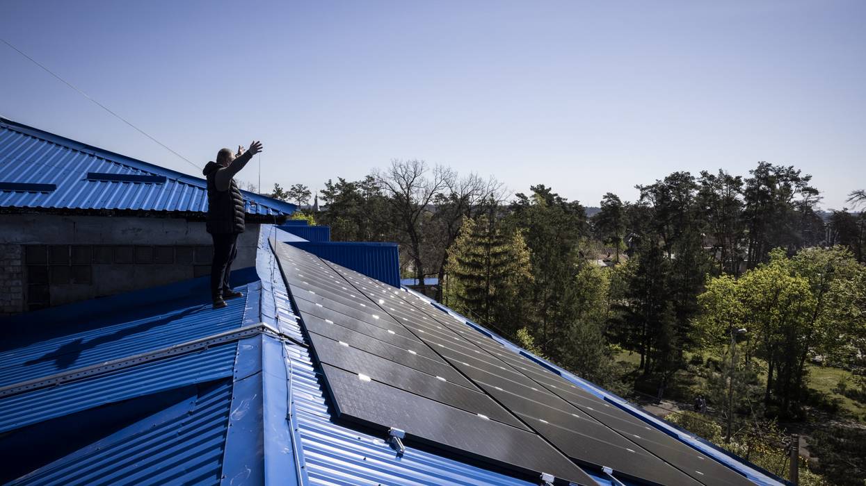 A principle waves to colleagues from a roof in Ukraine covered in solar panels.