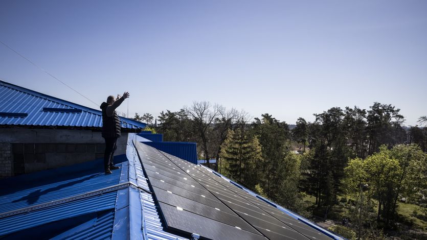 A principle waves to colleagues from a roof in Ukraine covered in solar panels.